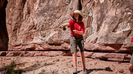 Girl in a hate casting fishing pole into a river