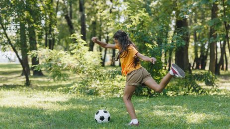 side view of girl kicking soccer ball in park